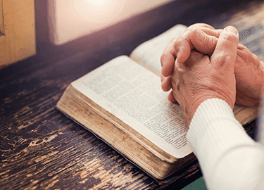 Hands in prayer over an open Bible